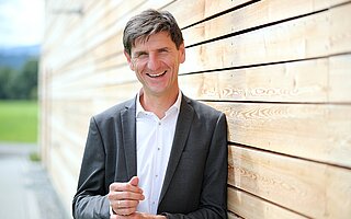 Gerhard Frey steht vor einer Holzwand.